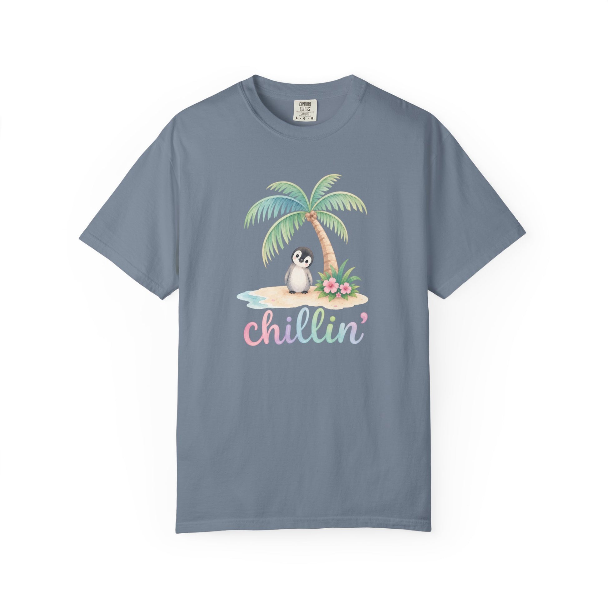 A slate blue crewneck t-shirt featuring a tropical graphic of a penguin sitting under a palm tree on a small beach with the word 'chillin'' written below in pastel pink and blue letters, displayed on a clean white background.