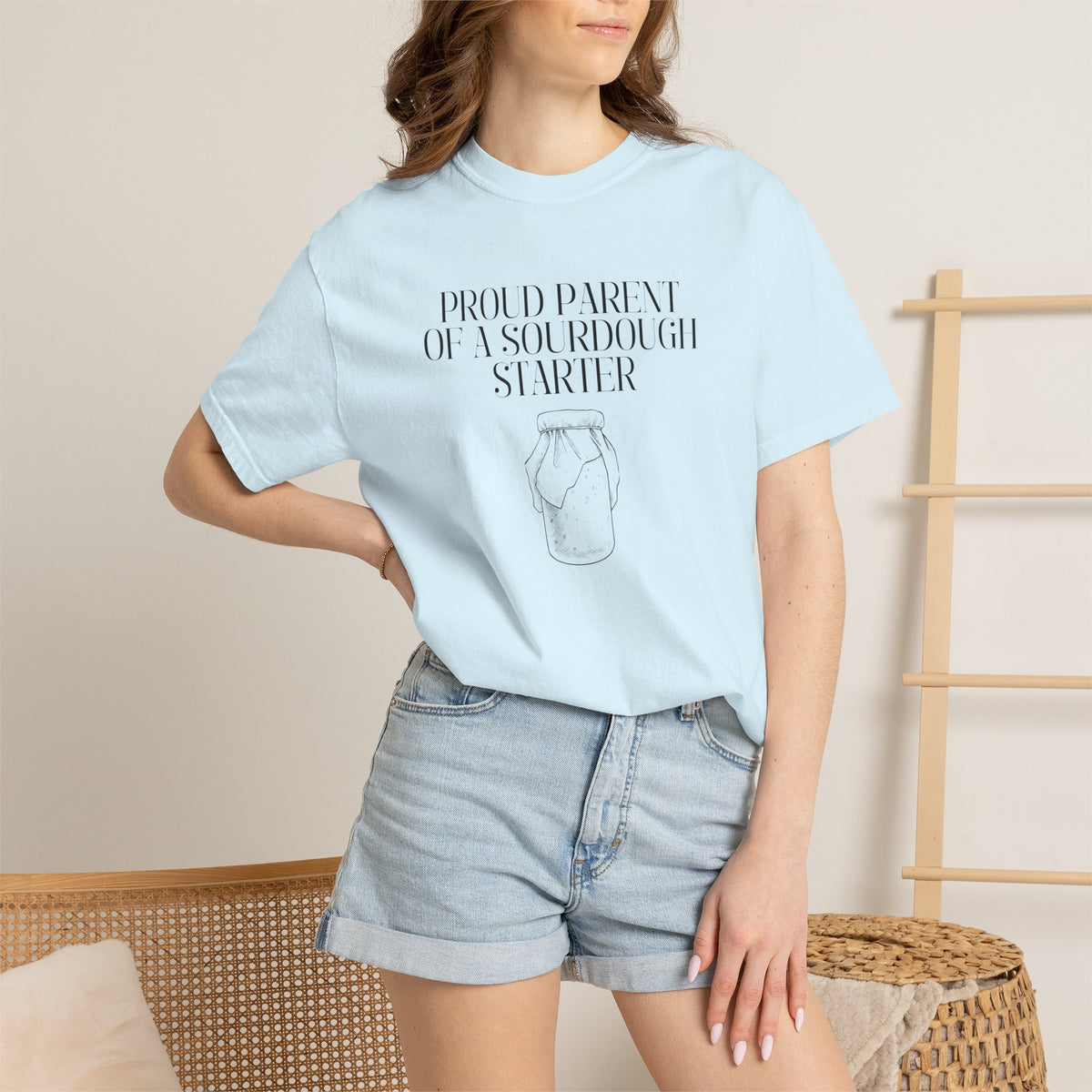 Model standing and wearing a light blue Comfort Colors® "Proud Parent of a Sourdough Starter" t-shirt with vintage sourdough jar graphic. Funny sourdough shirt for bakers, bread makers, and homemade bread enthusiasts.
