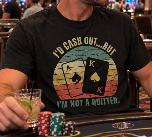 Man playing blackjack at a casino wearing a funny graphic tshirt that says “I’d cash out, but I’m not a quitter” with a retro sunset design featuring an ace and king of spades 
