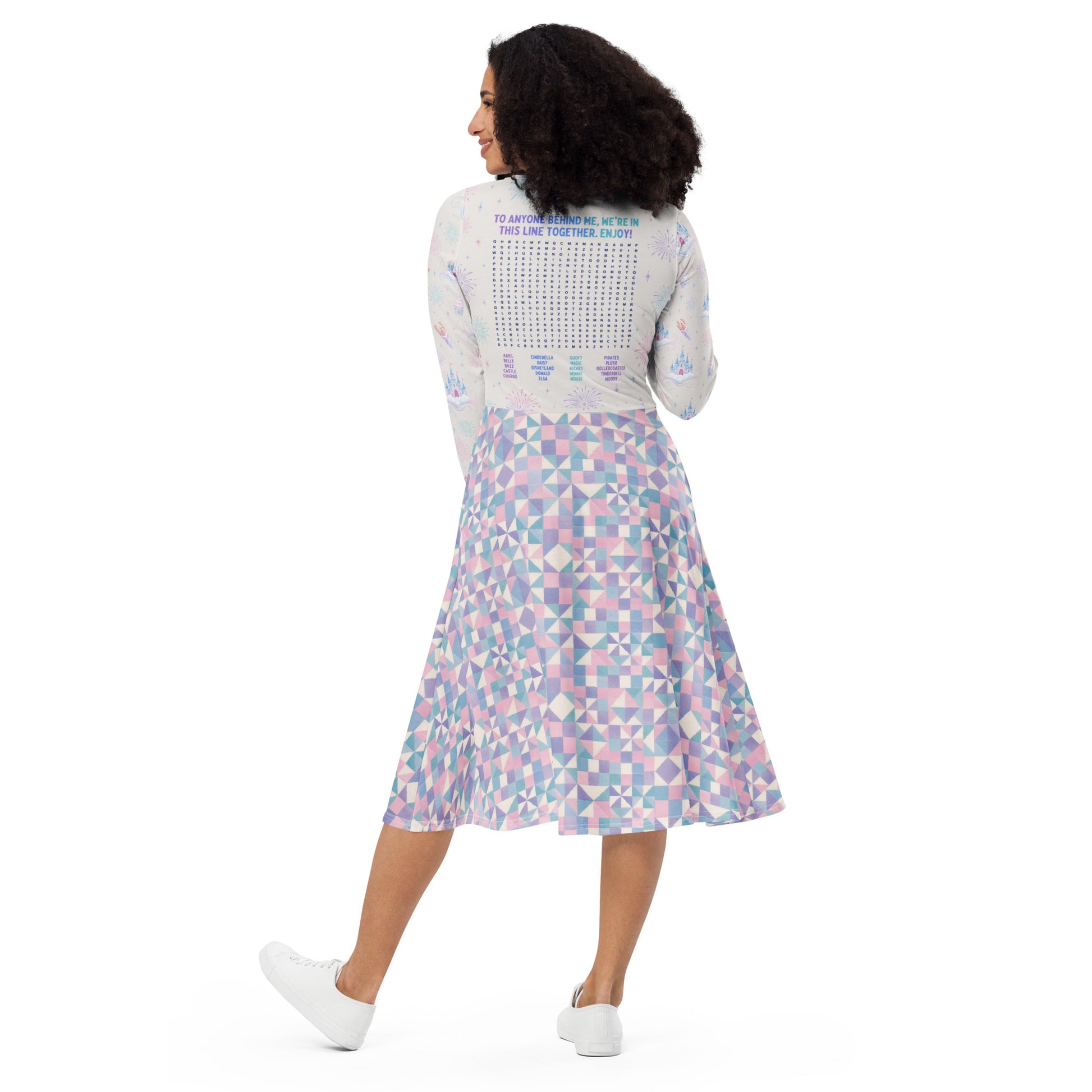 A woman is shown from behind wearing a long-sleeve midi dress with a Disneyland themed word search puzzle on the back and a pastel geometric print skirt in pink, blue, and purple, paired with white sneakers on a white background.