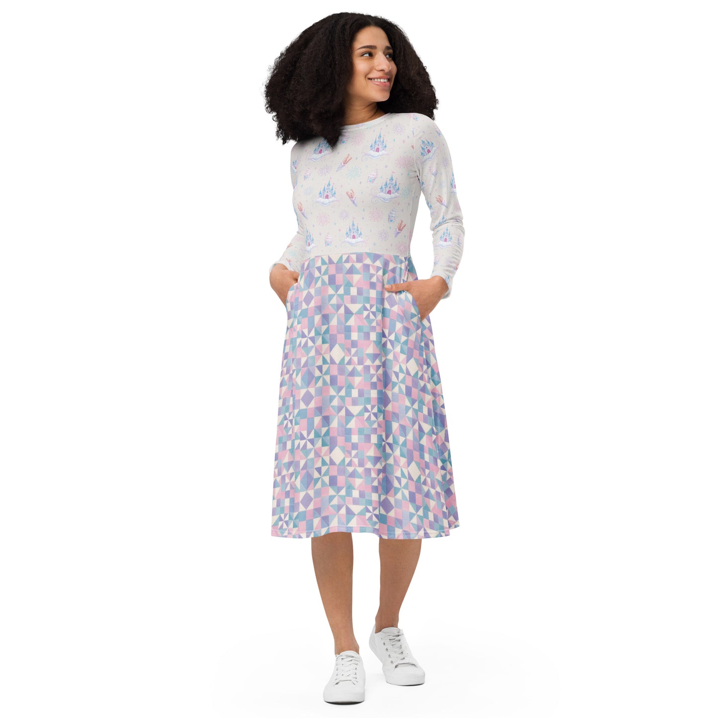 A woman modeling a long-sleeve midi dress with castles, churros, fireworks and ice cream scattered across the top and  a geometric skirt pattern in pastel pink, blue, and purple on a white base, paired with white sneakers, against a plain white background.