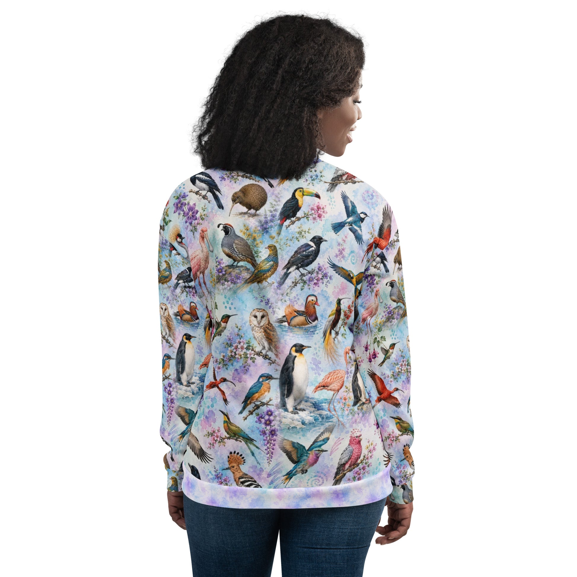 A woman shown from the back wearing a long-sleeve zip-up hoodie with an all-over colorful bird print on a light pastel background, paired with dark blue jeans against a plain white studio background.
