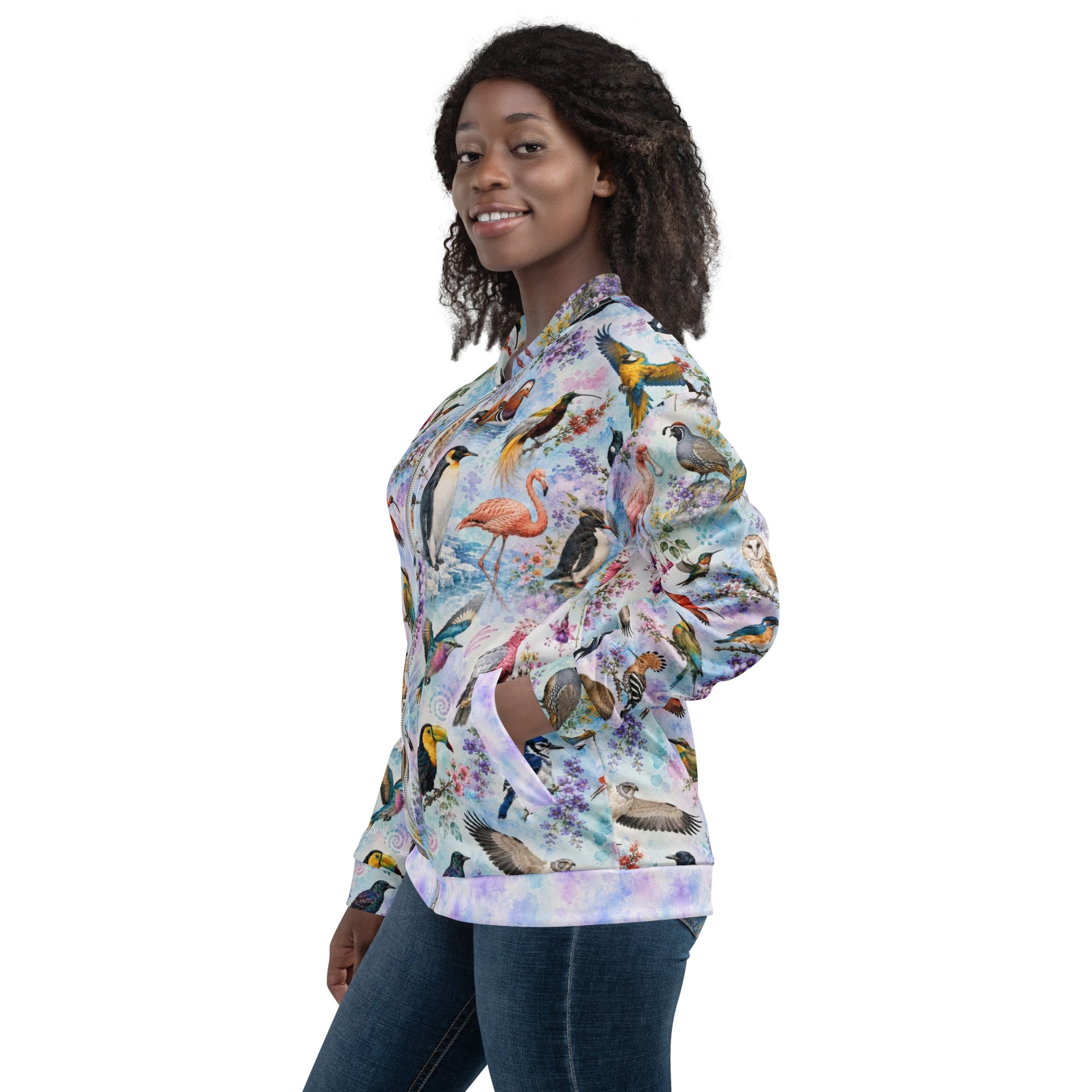 A woman modeling a long-sleeve bomber jacket with a colorful tropical bird print, paired with blue jeans, against a plain white background.