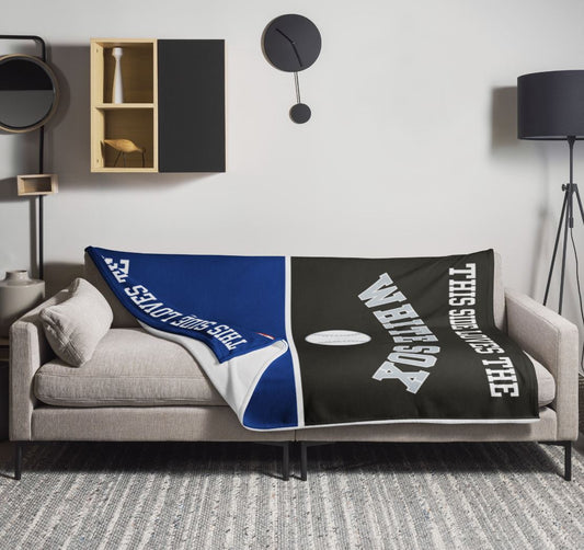Personalized house divided baseball throw blanket draped over a couch in a modern living room, the blue Cubs side folded to show its white reverse beside the black White Sox side.