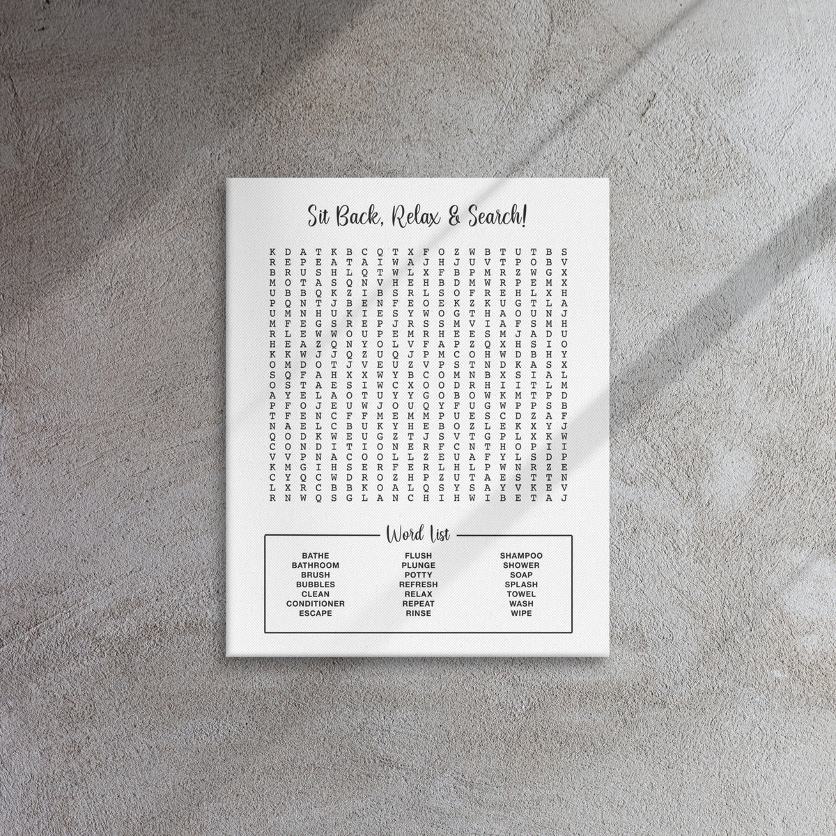 A white wrapped canvas art design featuring a bathroom themed word search puzzle print against a light gray background. The print reads 'Sit Back, Relax & Search!' with a grid of letters and a word list at the bottom including bath, brush, shower, soap, towel, wash, and more.