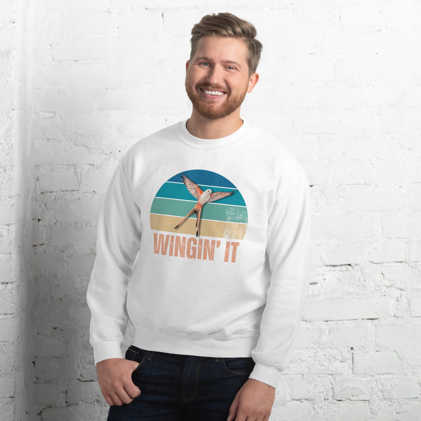 Smiling man in a white Wingin' It crewneck sweatshirt with a Wingspan-inspired scissor-tailed flycatcher and retro sunset design