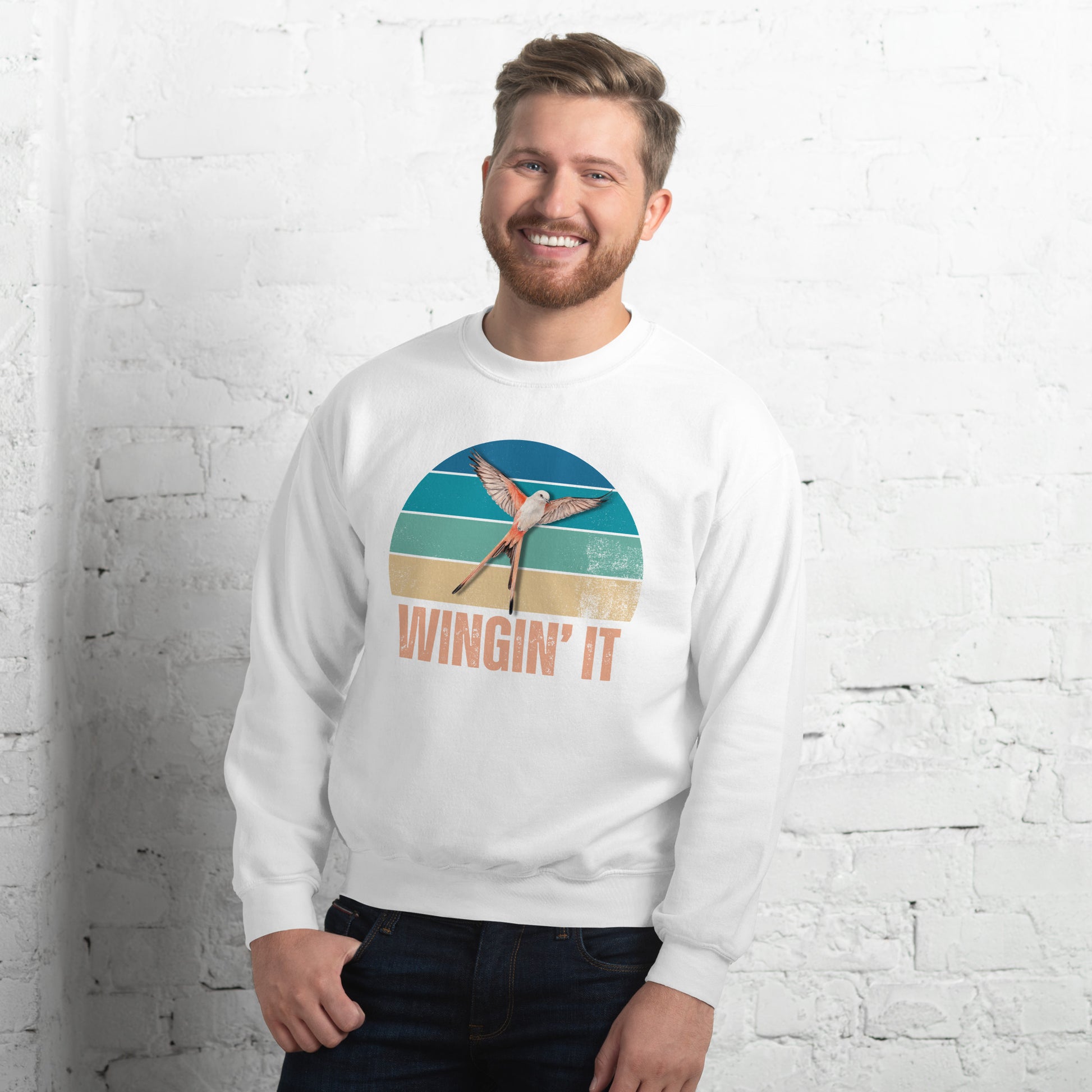 Smiling man in a white Wingin' It crewneck sweatshirt with a Wingspan-inspired scissor-tailed flycatcher and retro sunset design