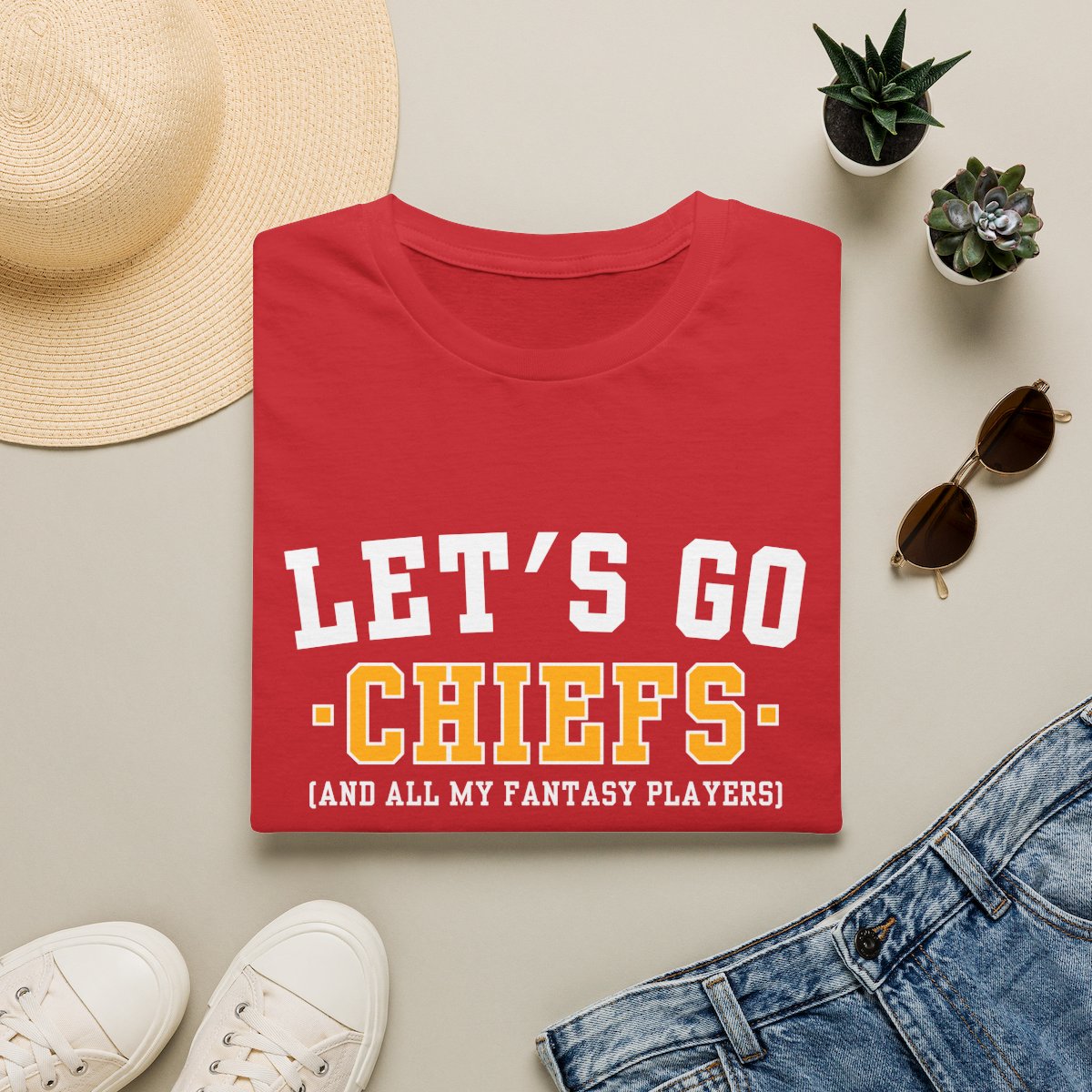 Red Chiefs fantasy football tee folded on a neutral flat lay with a straw hat and sneakers