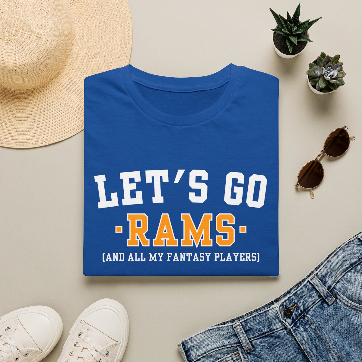 Royal blue Rams fantasy football tee folded on a neutral flat lay with a straw hat and sneakers