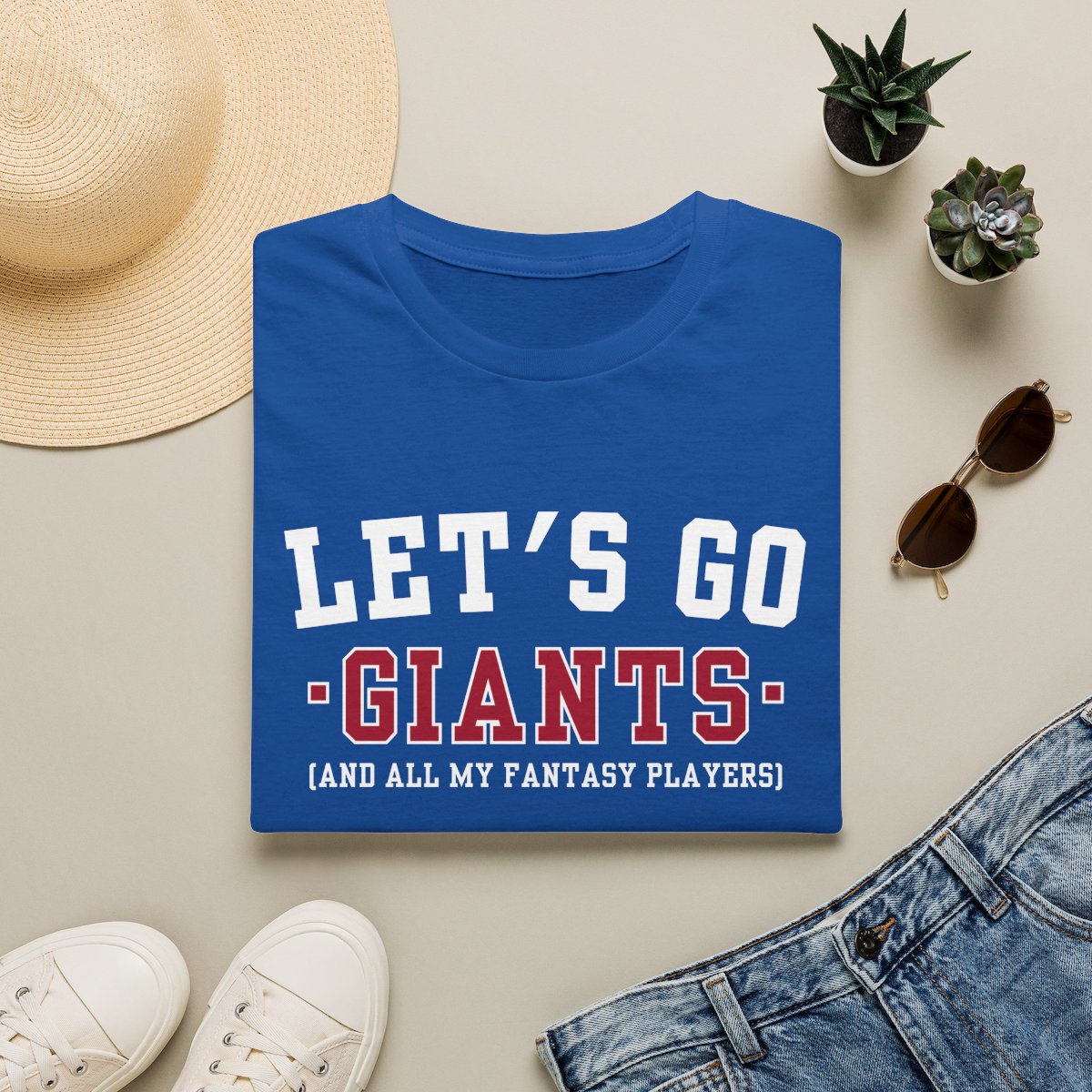 Royal blue Giants fantasy football tee folded on a neutral flat lay with a straw hat and sneakers