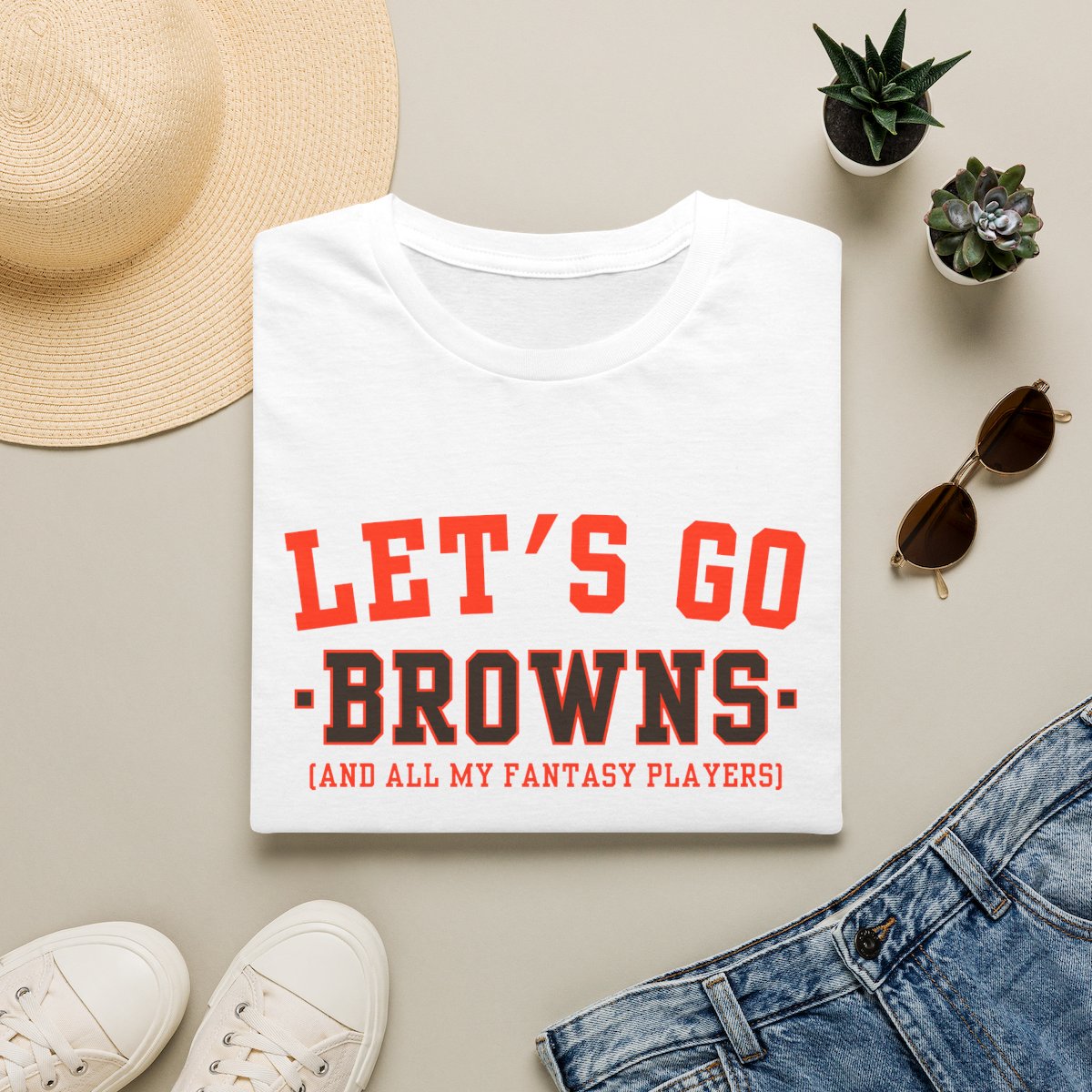 Orange Browns fantasy football tee folded on a neutral flat lay with a straw hat and sneakers