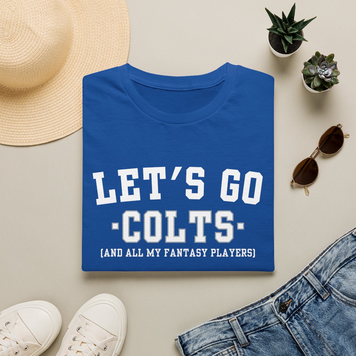 Royal blue Colts fantasy football tee folded on a neutral flat lay with a straw hat and sneakers