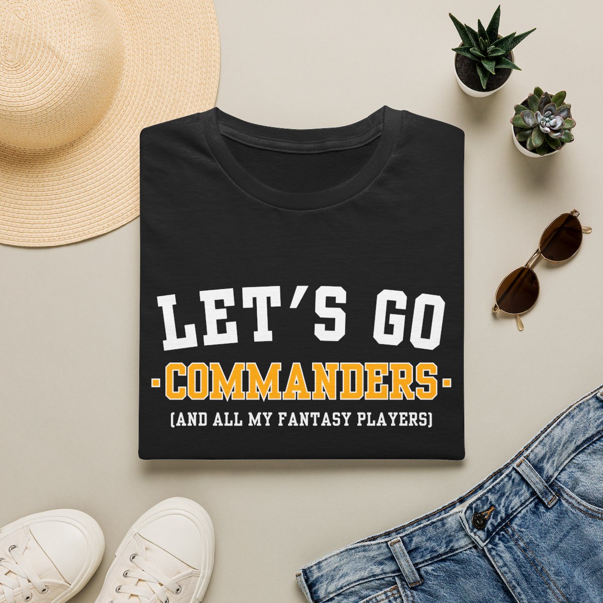Black Commanders fantasy football tee folded on a neutral flat lay with a straw hat and sneakers